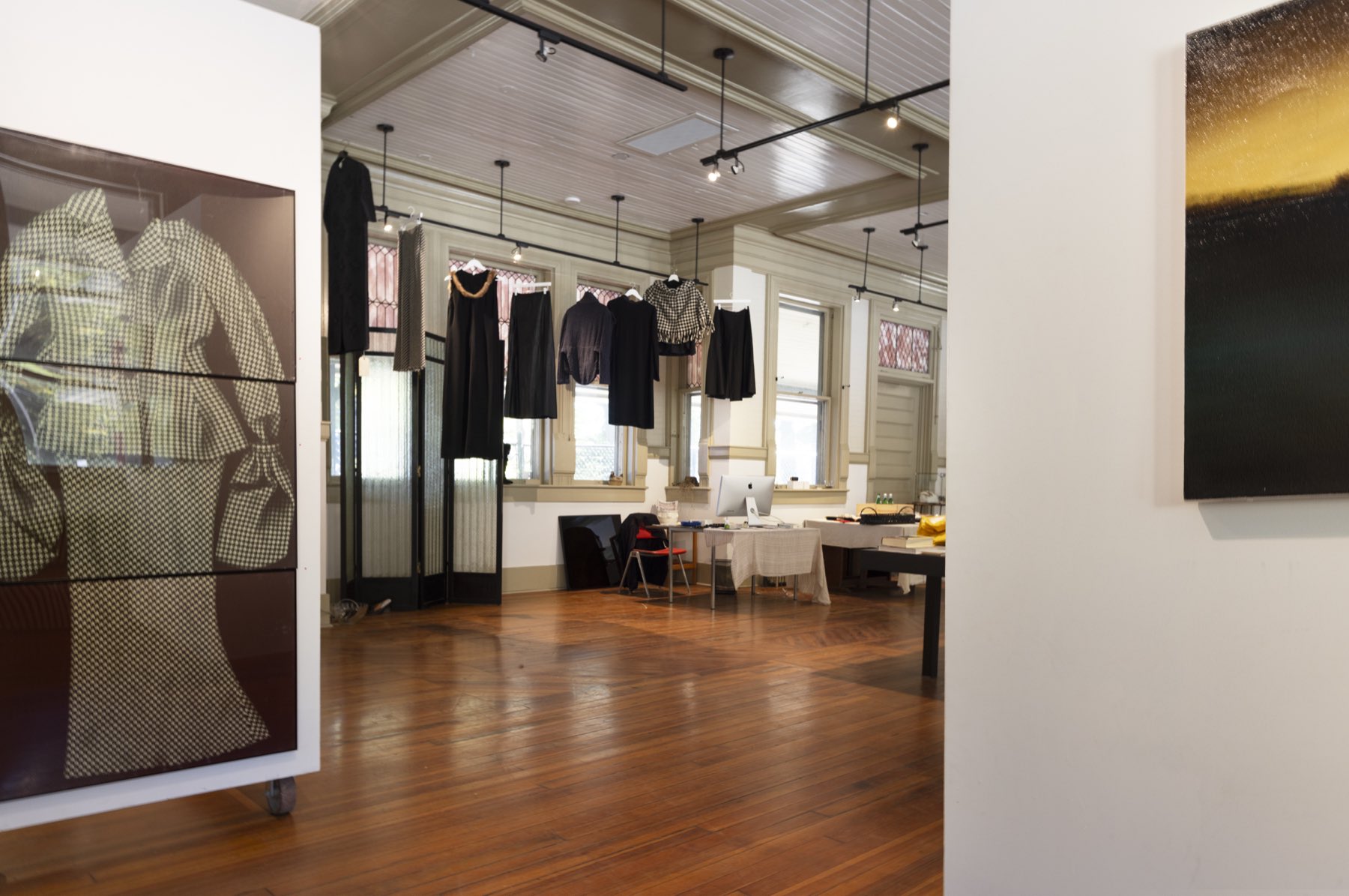Long gallery view with textiles, garments, paintings, and warm wooden floors.