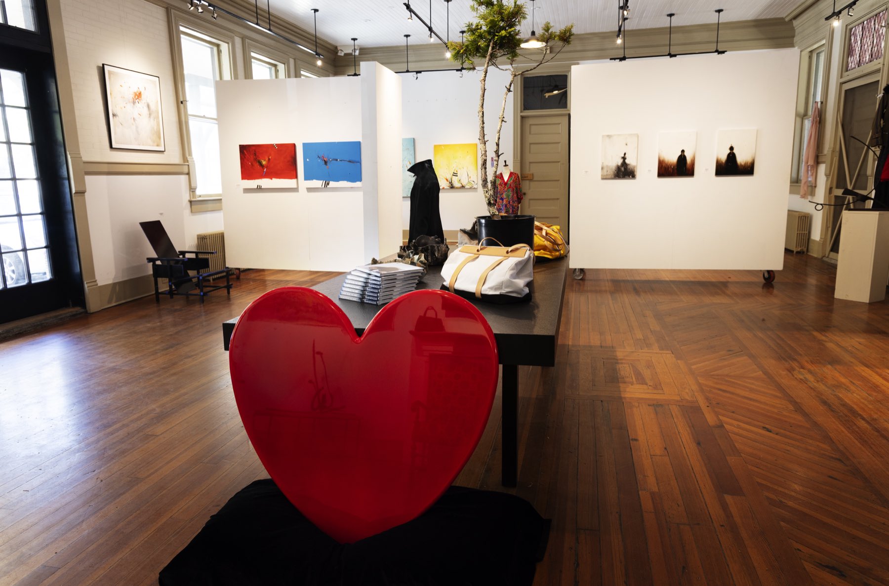 Red heart-shaped sculptural object anchoring a wide gallery installation.