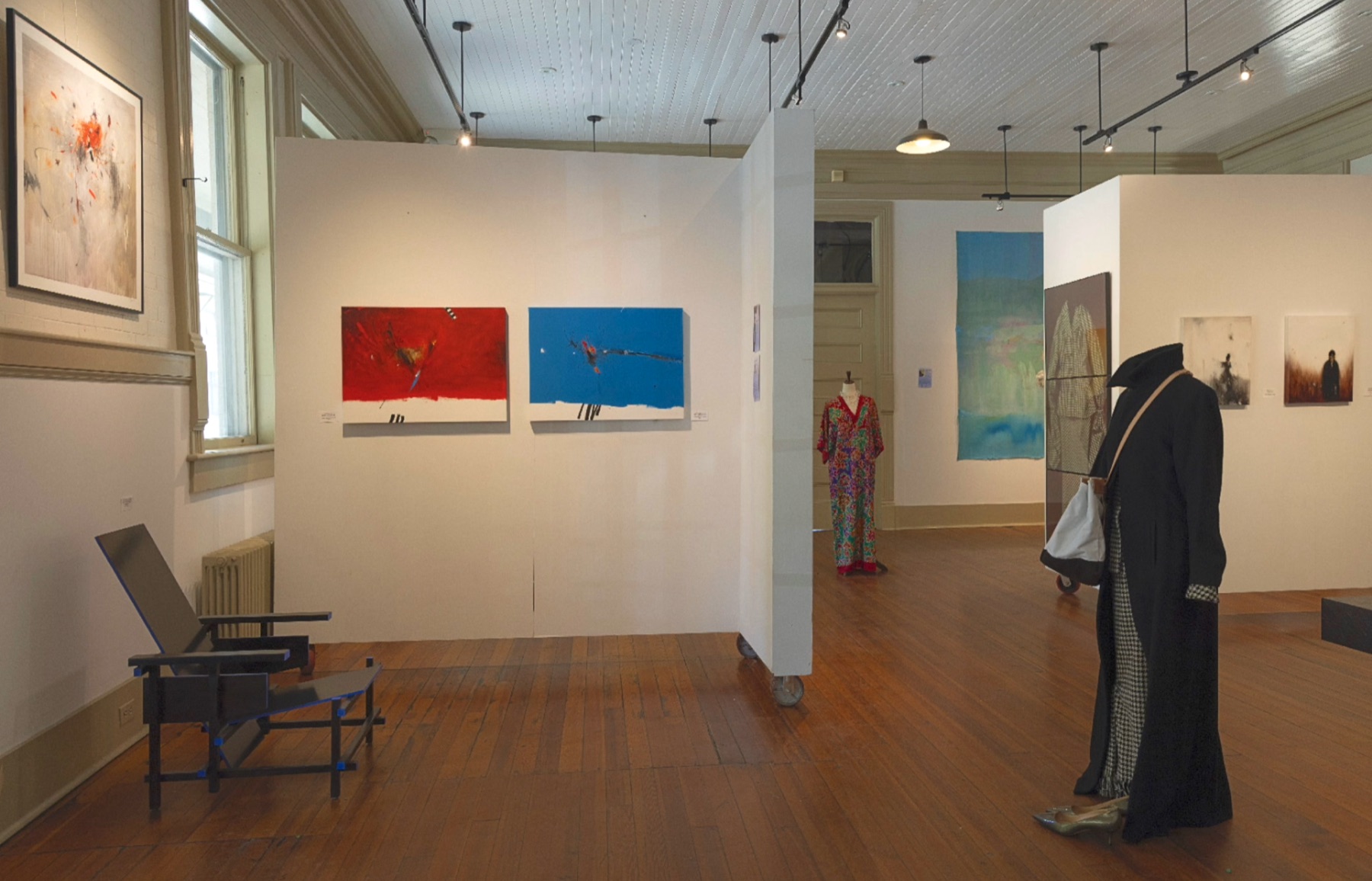 Interior gallery view with paintings, garments, and installation pieces.