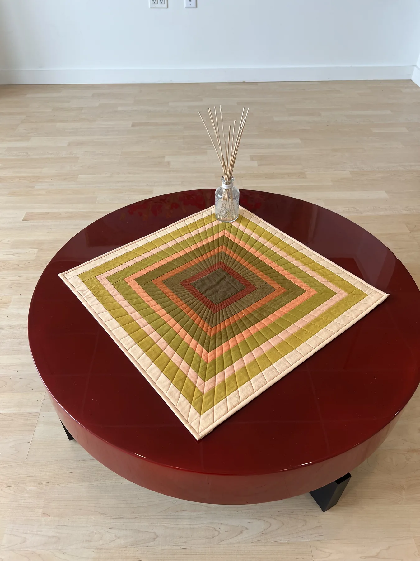 Red disc table displaying a geometric handmade quilt and glass vessel.