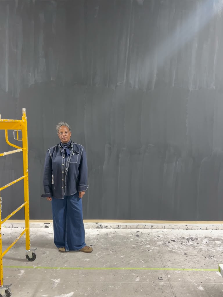 Samantha Dalmas standing in front of a charcoal-painted wall in a gallery installation space.